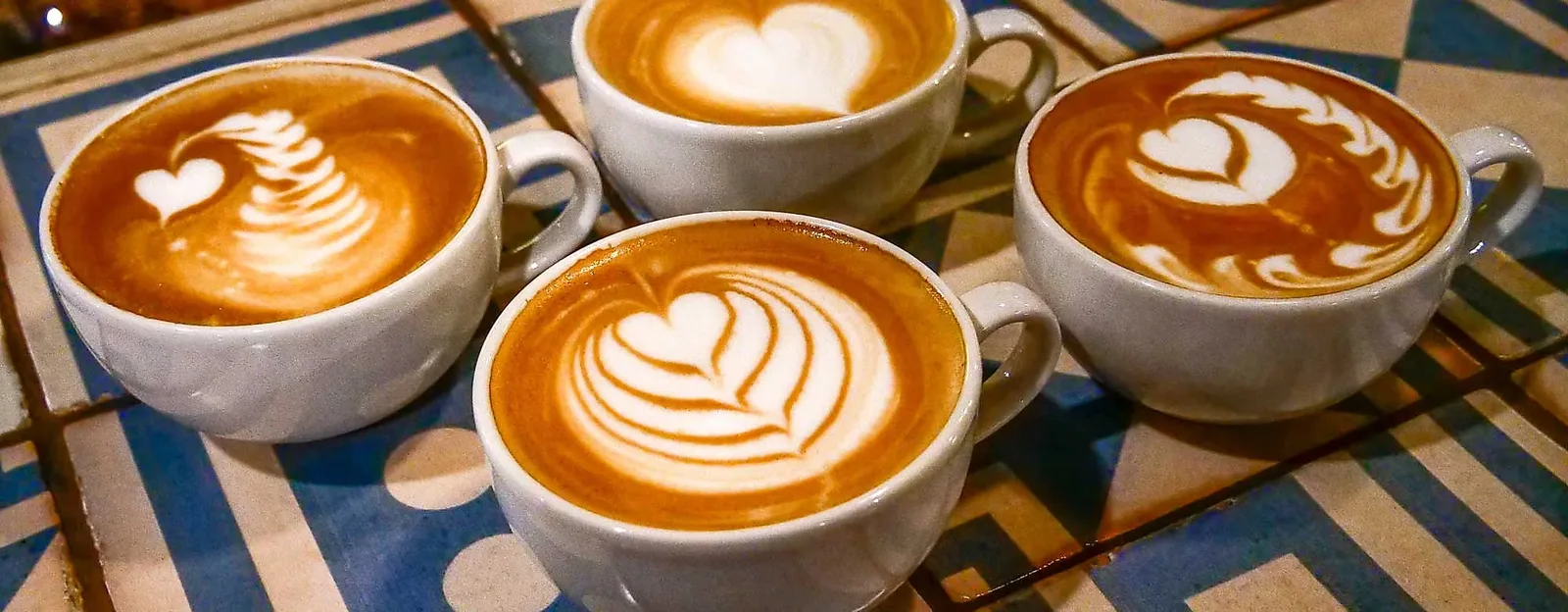 four white cups of latte art coffee arranged on a blue patterned table., kaffeemuseum burg, hamburg