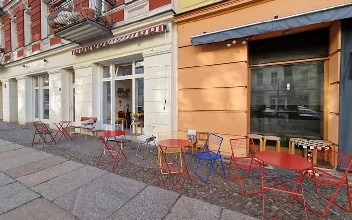 colorful outdoor café seating along european street with red tables and chairs., kajumi, berlin