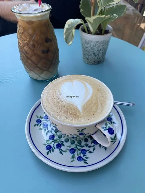 coffee cup with heart latte art, iced beverage, and potted plant on blue table., kazik amsterdam, amsterdam
