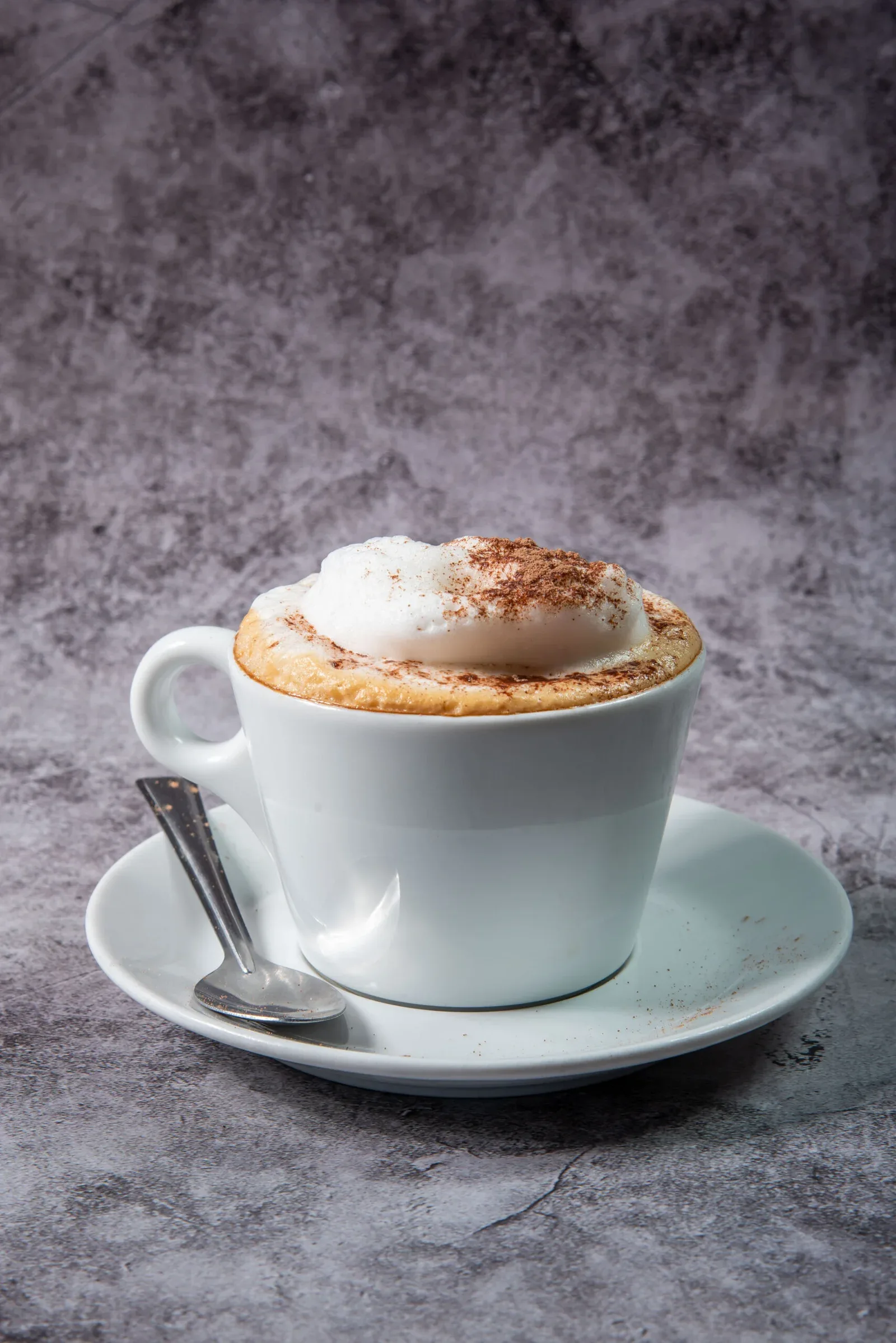 cappuccino with cinnamon-dusted foam and biscuit in white cup on saucer., kennington lane cafe, london
