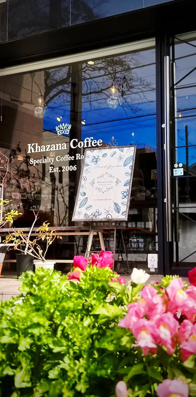 khazana coffee storefront with crown logo, established 2006, pink flowers foreground., khazana coffee, tokyo