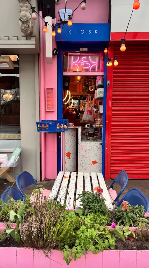 vibrant pink kiosk storefront with neon signage and hanging orange decorative lights., kiosk on lapwing, manchester