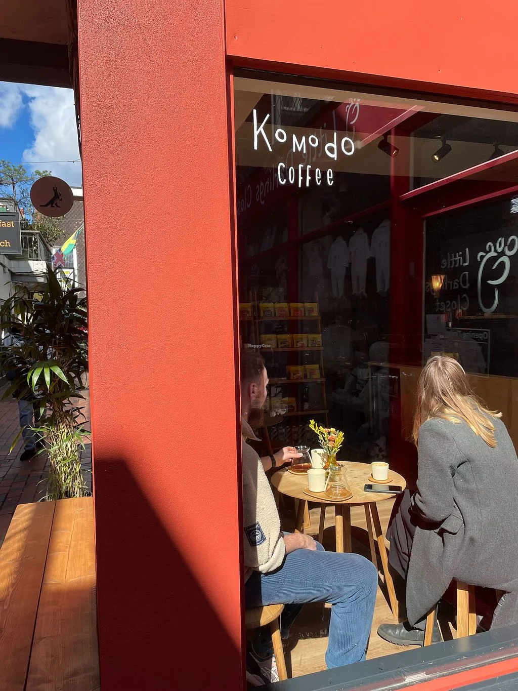 two people seated at wooden table inside komodo coffee cafe with red facade., komodo • specialty coffee brewers, brighton