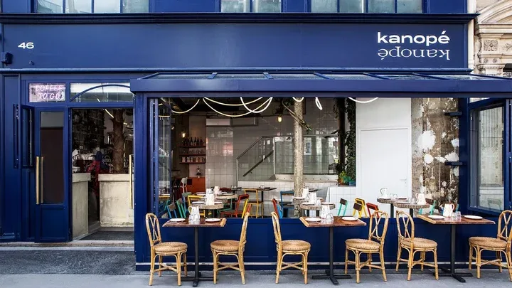 blue storefront restaurant with wicker chairs and dining tables outside., kozy, paris