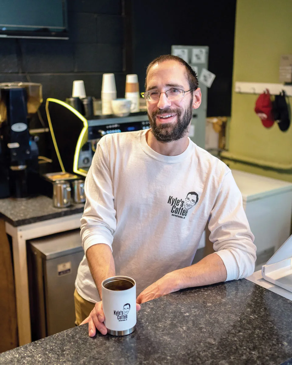man wearing kyle's coffee sweatshirt holds branded mug in coffee shop., kyle’s coffee, kernersville