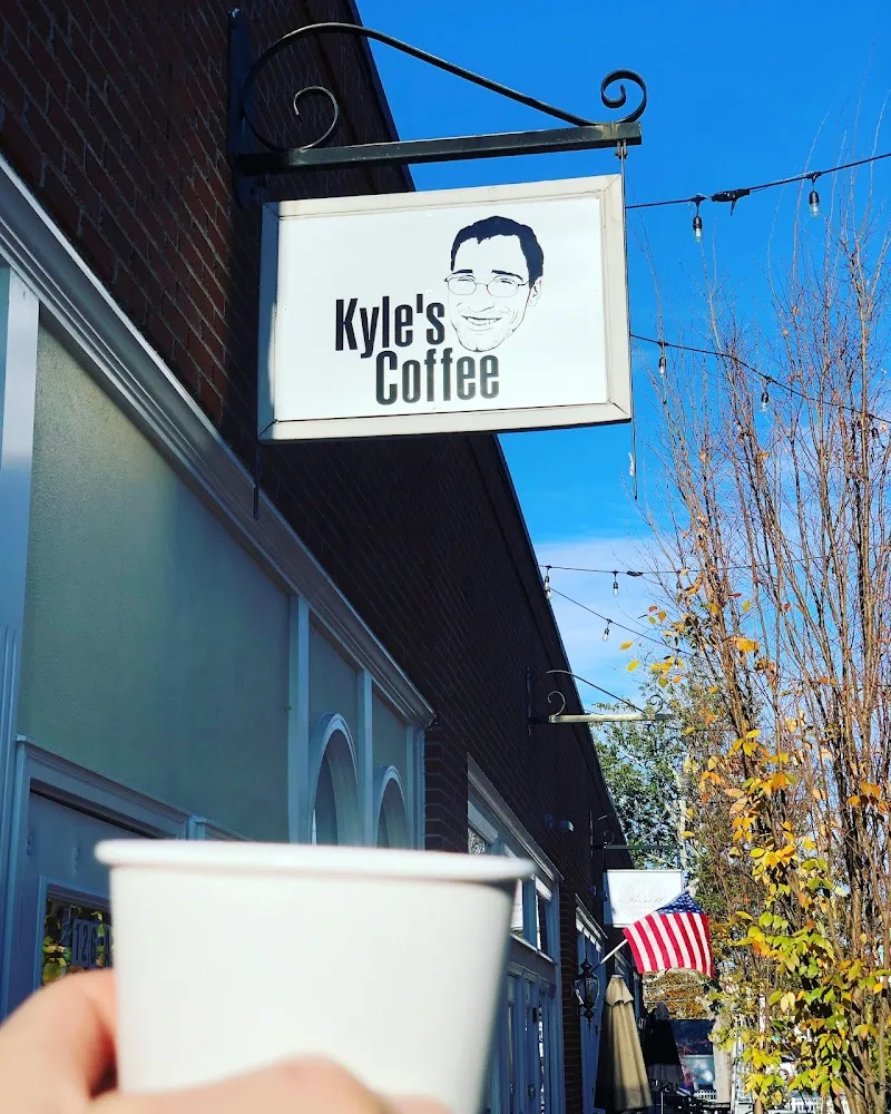 kyle's coffee storefront sign with white cup held in foreground, autumn foliage visible., kyle’s coffee, kernersville