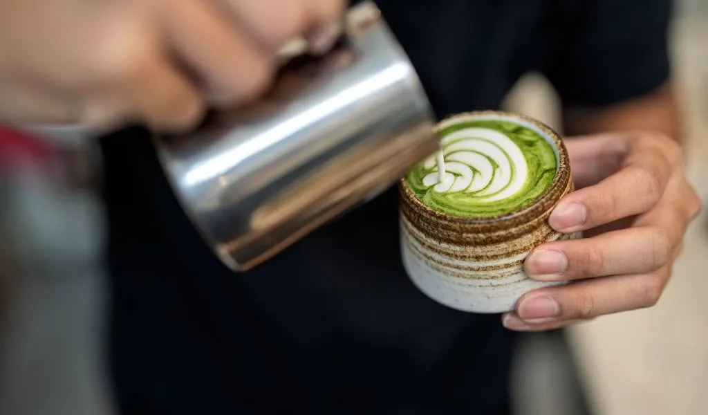 barista holding matcha latte with white latte art design in ceramic cup., kyoto match good, jung district