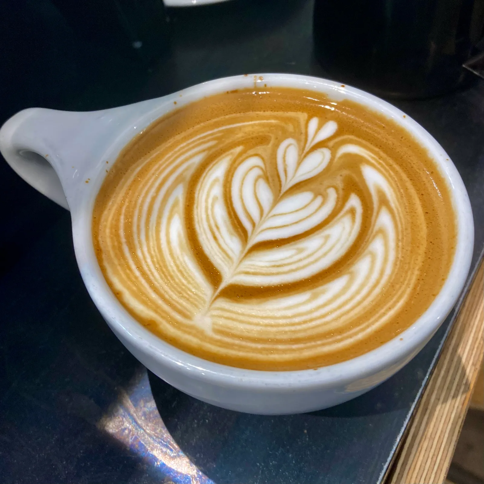 latte with intricate leaf latte art in white ceramic cup on dark surface., latte'liê art in coffee, são paulo