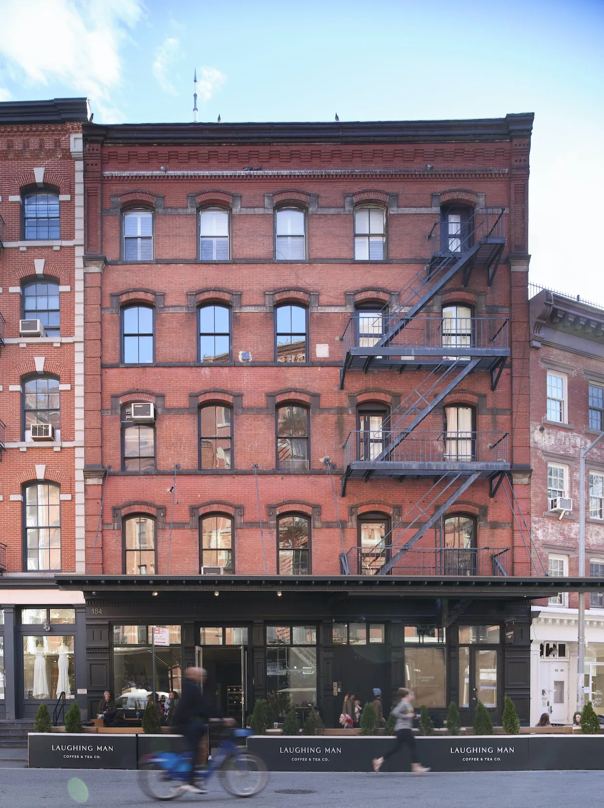 red brick building with fire escapes and street-level coffee shop storefront., laughing man coffee, new york