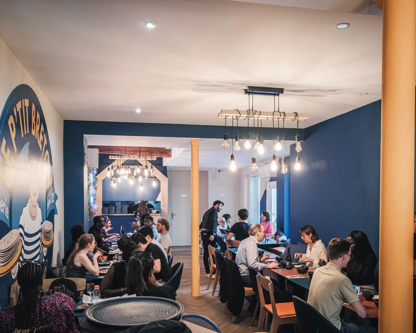 modern restaurant interior with blue walls, pendant lighting, and diners seated at tables., le p'tit breton | lorette, paris