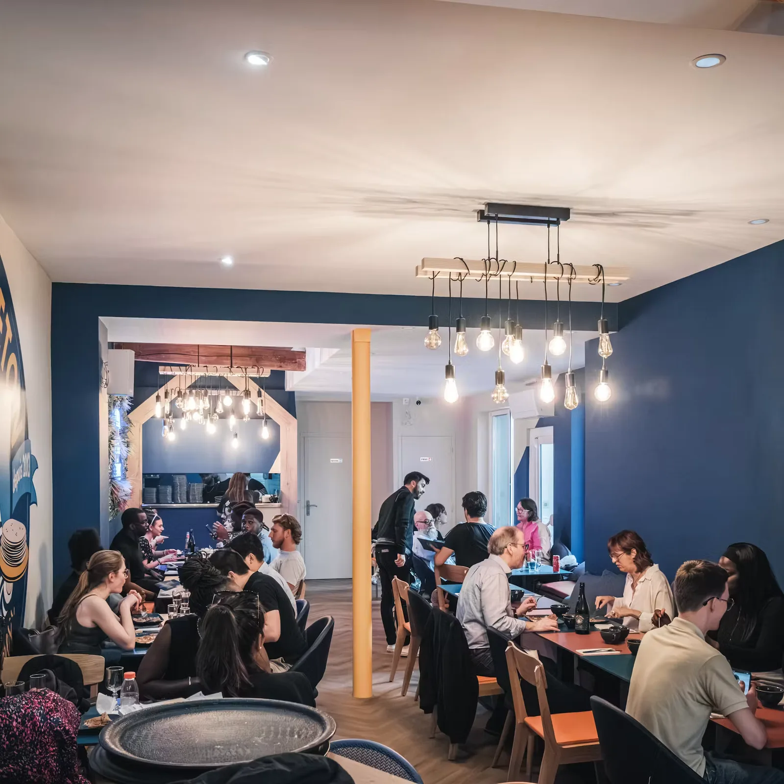 modern restaurant interior with blue walls, pendant lighting, and diners seated at tables., le p'tit breton | opéra, paris