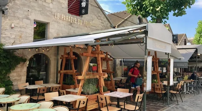outdoor café with retractable awning, wooden furniture, and stone building facade., le paradis du fruit, paris