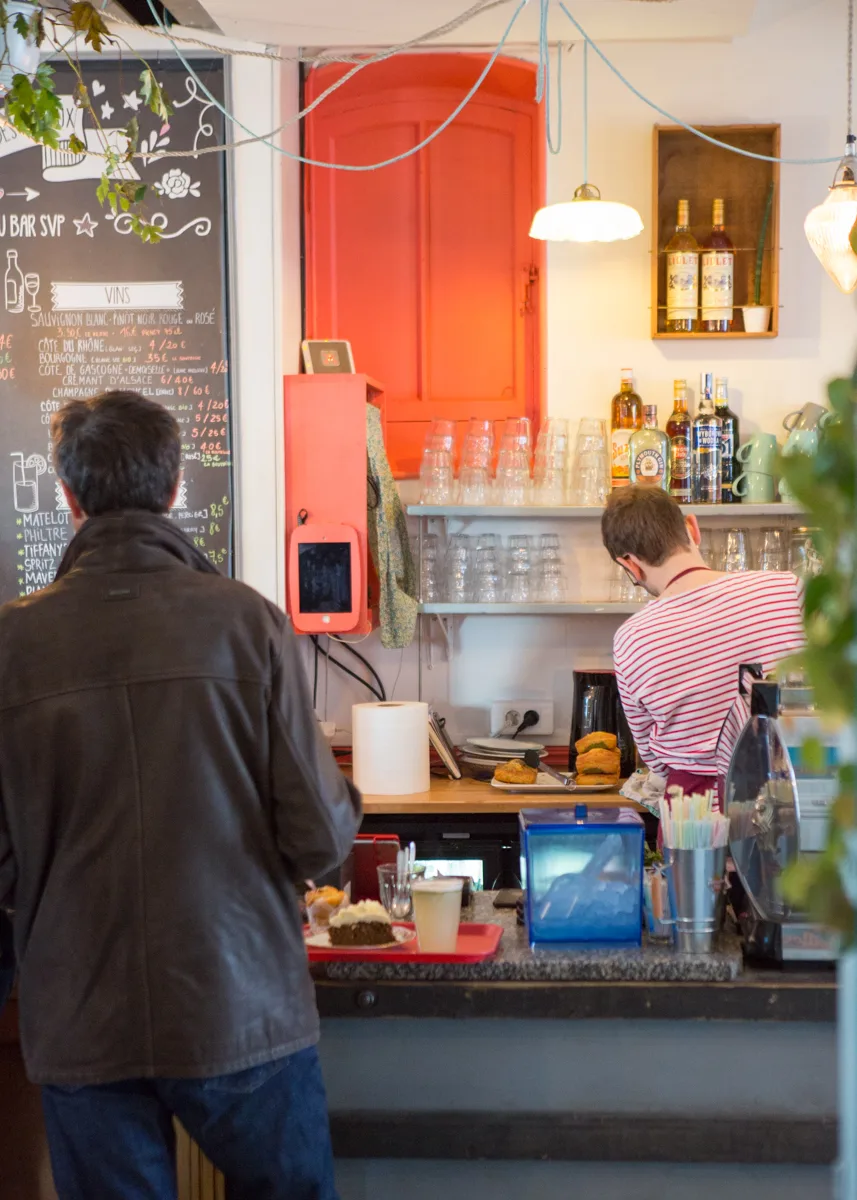 small wine bar with customer ordering, bright red door, chalkboard menu, hanging lights., le pavillon des canaux, paris