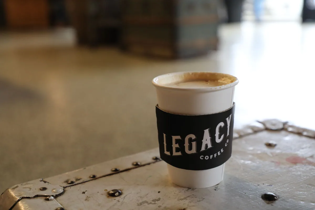 legacy coffee cup with black sleeve on concrete surface with scattered beans., legacy coffee co., columbia