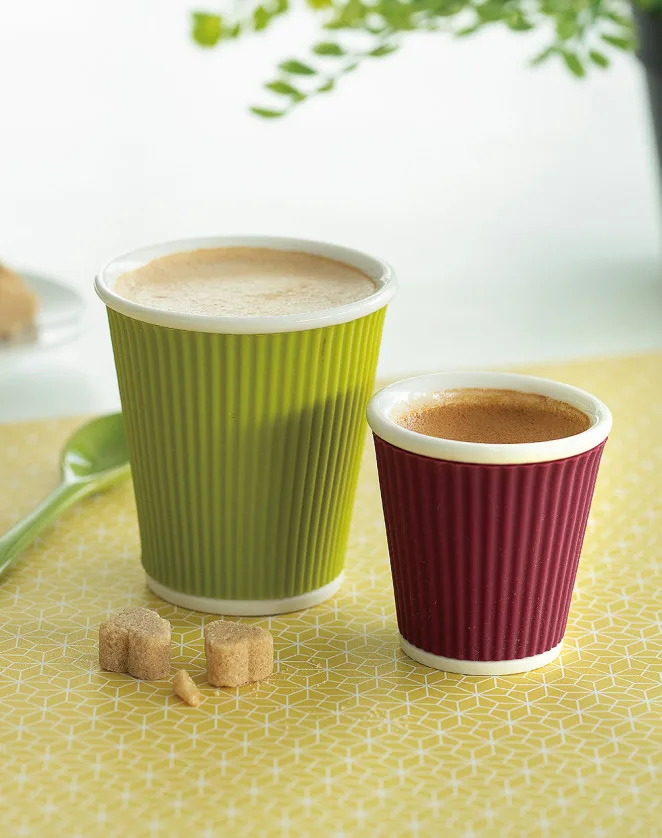 two coffee cups with corrugated sleeves on yellow patterned surface with sugar cubes., les artistes, paris