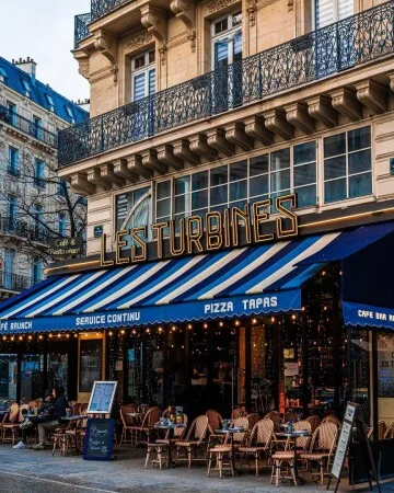 parisian café storefront with blue striped awning and outdoor seating area., les turbines, paris