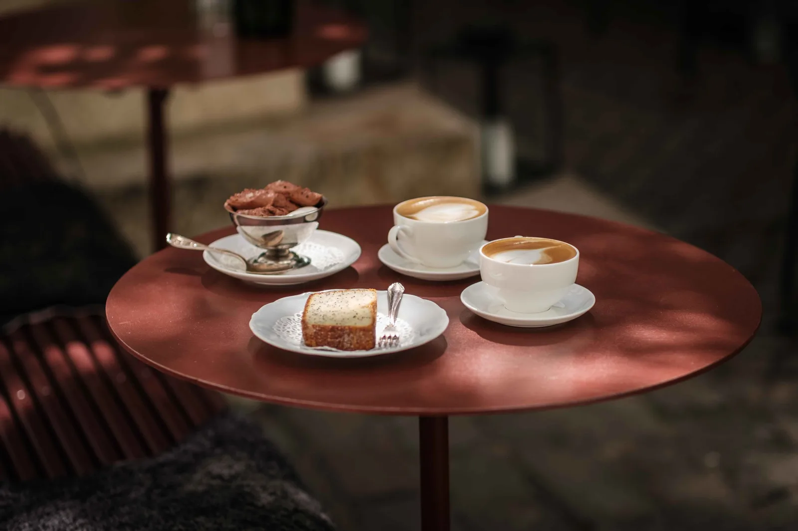 red round table with coffee cups, cake slice, and chocolate treats outdoors., leymans café, gothenburg