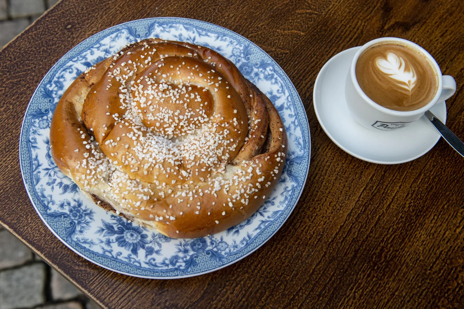 pretzel with coarse salt on blue porcelain plate, cappuccino with latte art beside it., leymans café, gothenburg