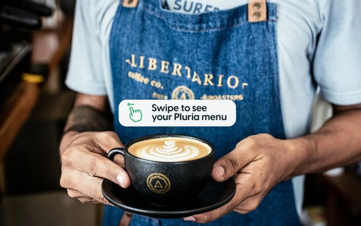 barista in denim apron holding latte with latte art design., libertario coffee roasters cartagena, cartagena