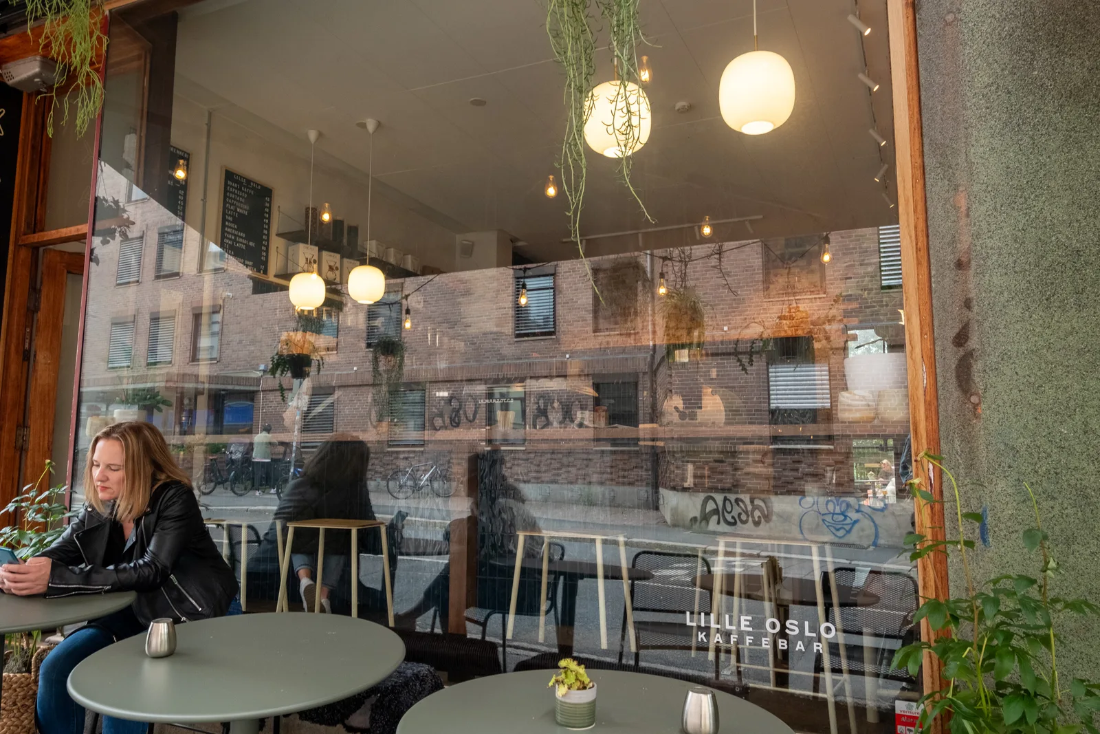 woman sitting at café table with view of brick building through window., lille oslo kaffebrenneri, oslo