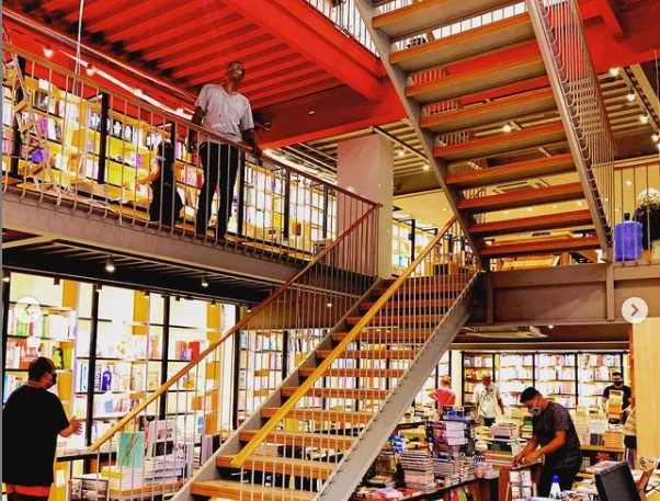 multi-level bookstore with red ceiling, wooden stairs, and yellow window displays., livraria da travessa - icaraí, niterói