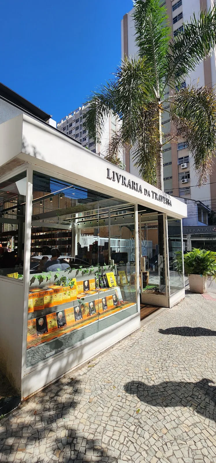 white bookstore kiosk "livraria da travessa" with palm trees and urban buildings., livraria da travessa - icaraí, niterói