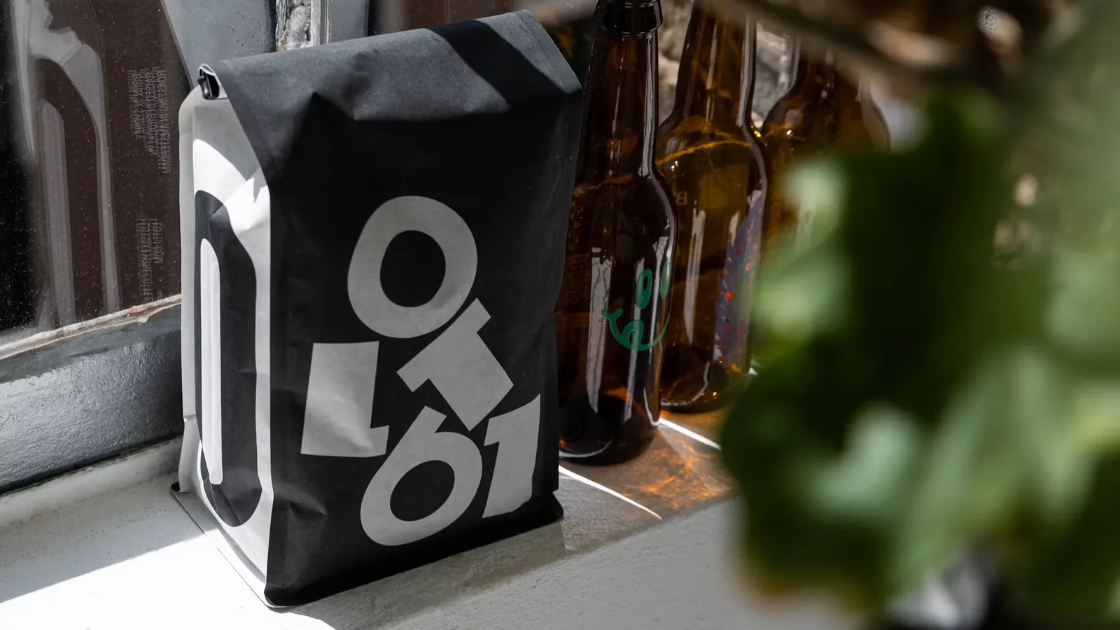 black bag with geometric logo beside beer bottles on windowsill., lot61 coffee roasters, amsterdam