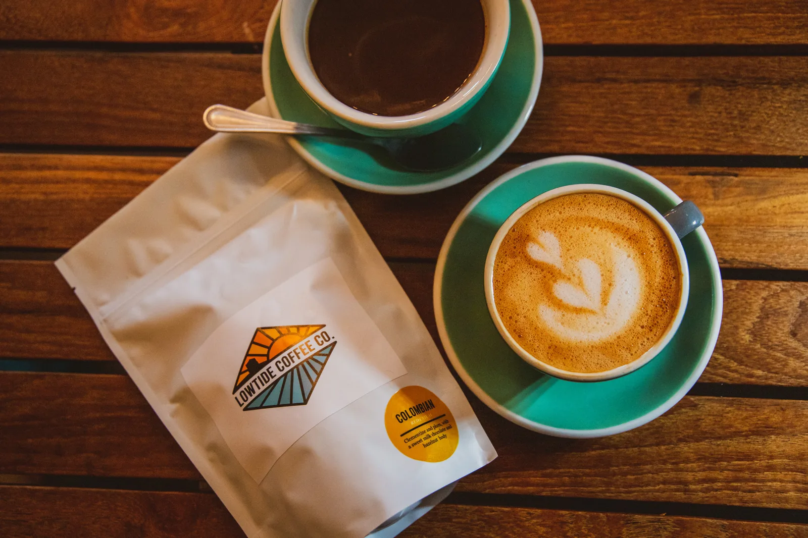 two green and white cups of coffee beside a bag of bayside coffee co colombian beans., low tide coffee roasters, san diego