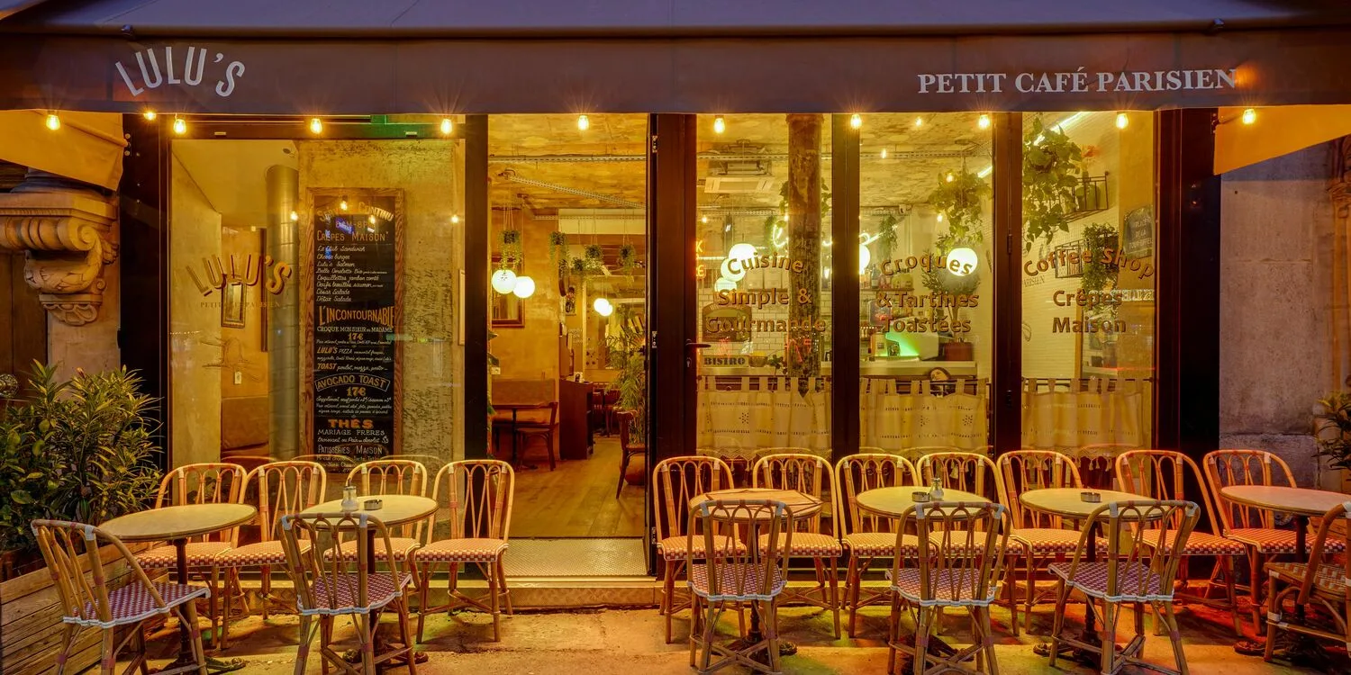 parisian café storefront at night with wicker chairs and warm interior lighting., lulu's, paris