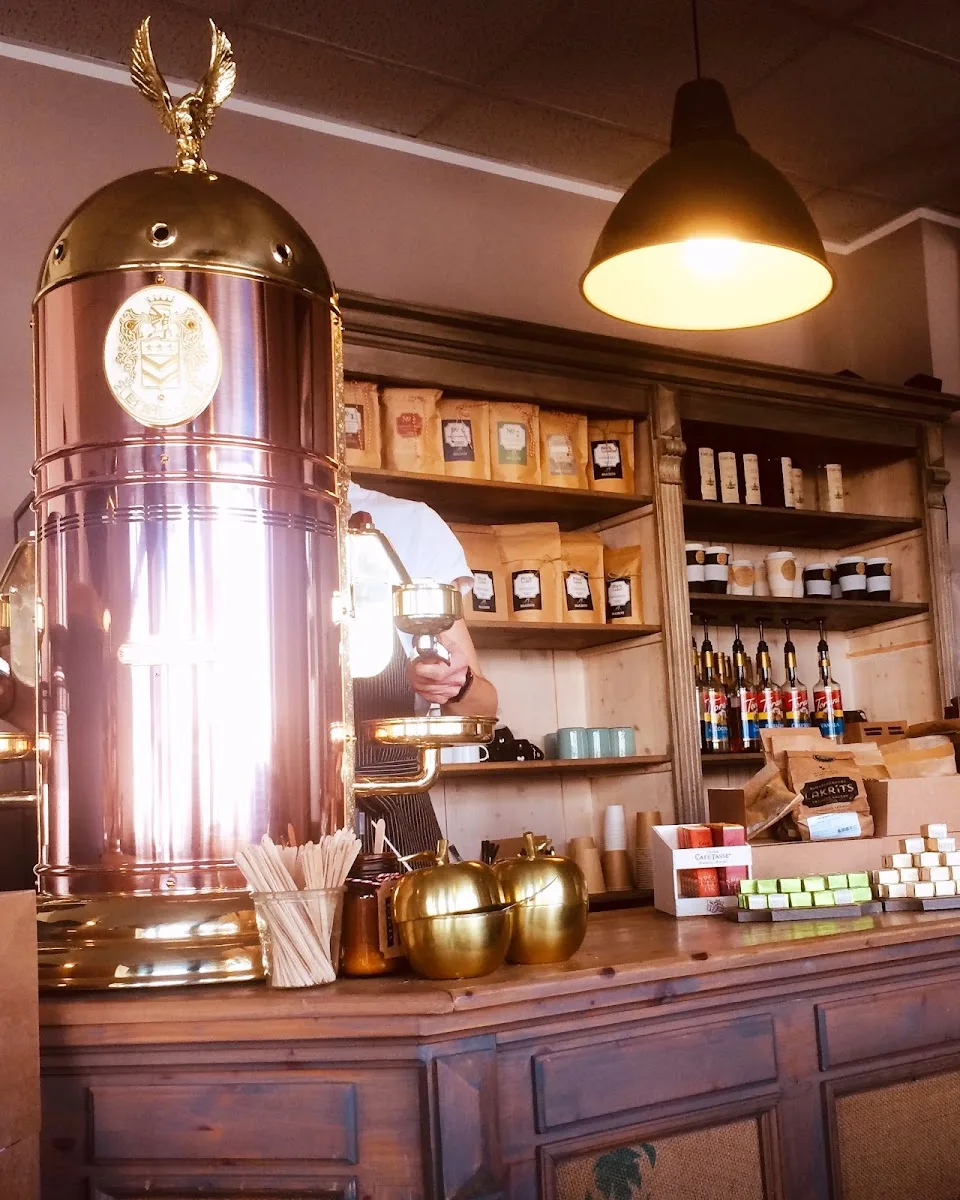 luxurious coffee shop counter with gleaming rose gold espresso machine and golden decorative apples., mahou-kaffeerösterei, c