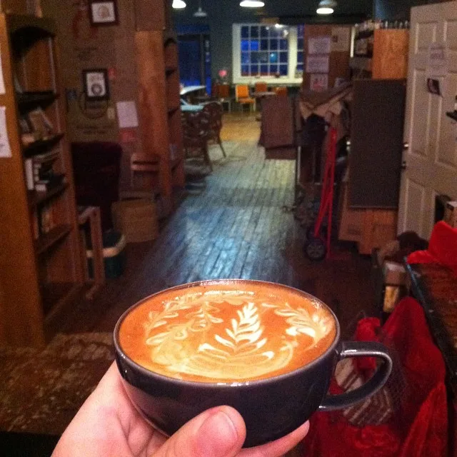 hand holding black cup with latte art in cozy coffee shop interior., mama mocha's coffee emporium & roasters, opelika