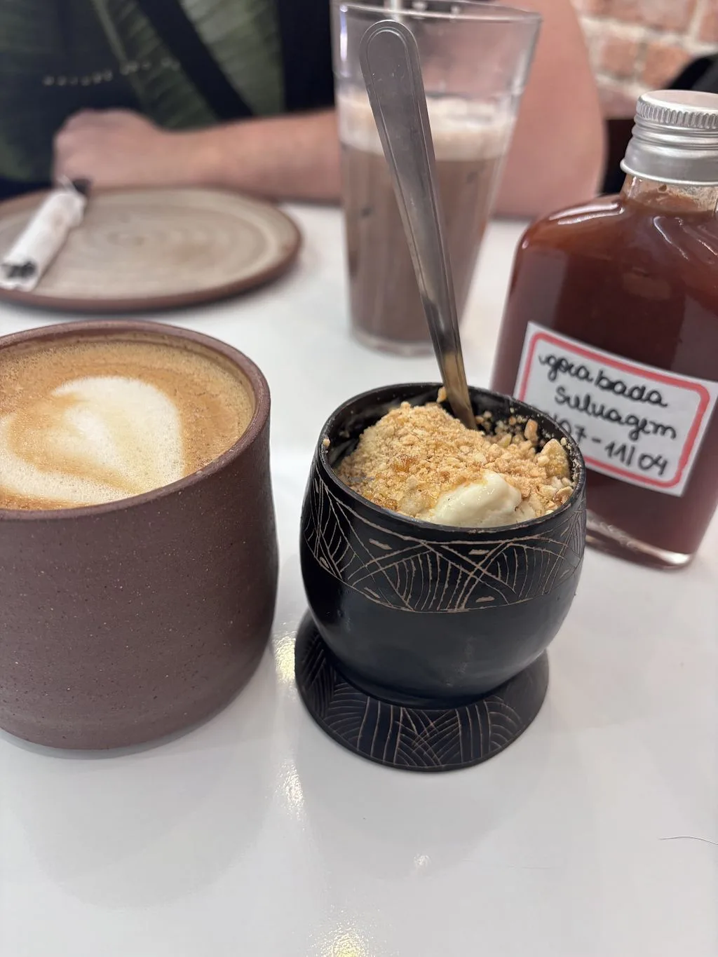 coffee cup with latte art beside a dessert in a black decorative bowl., manifesto café, curitiba