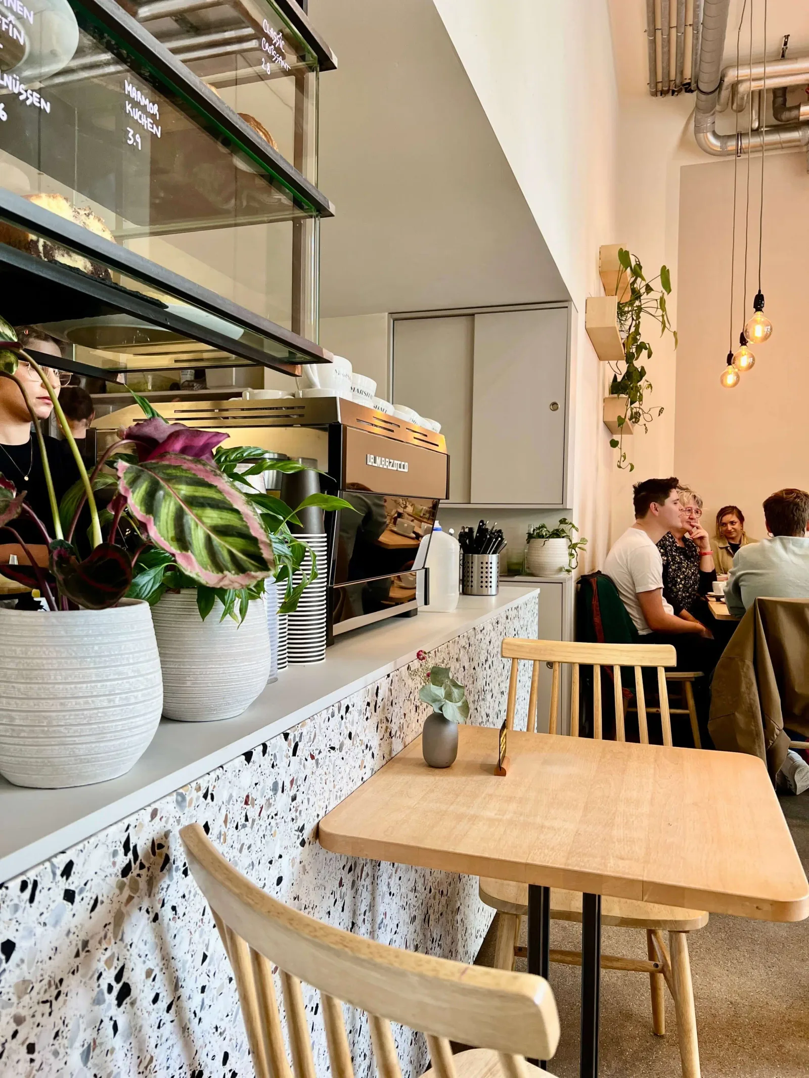 modern café interior with wooden tables, potted plants, and customers seated at counter., marshall street coffee, hamburg
