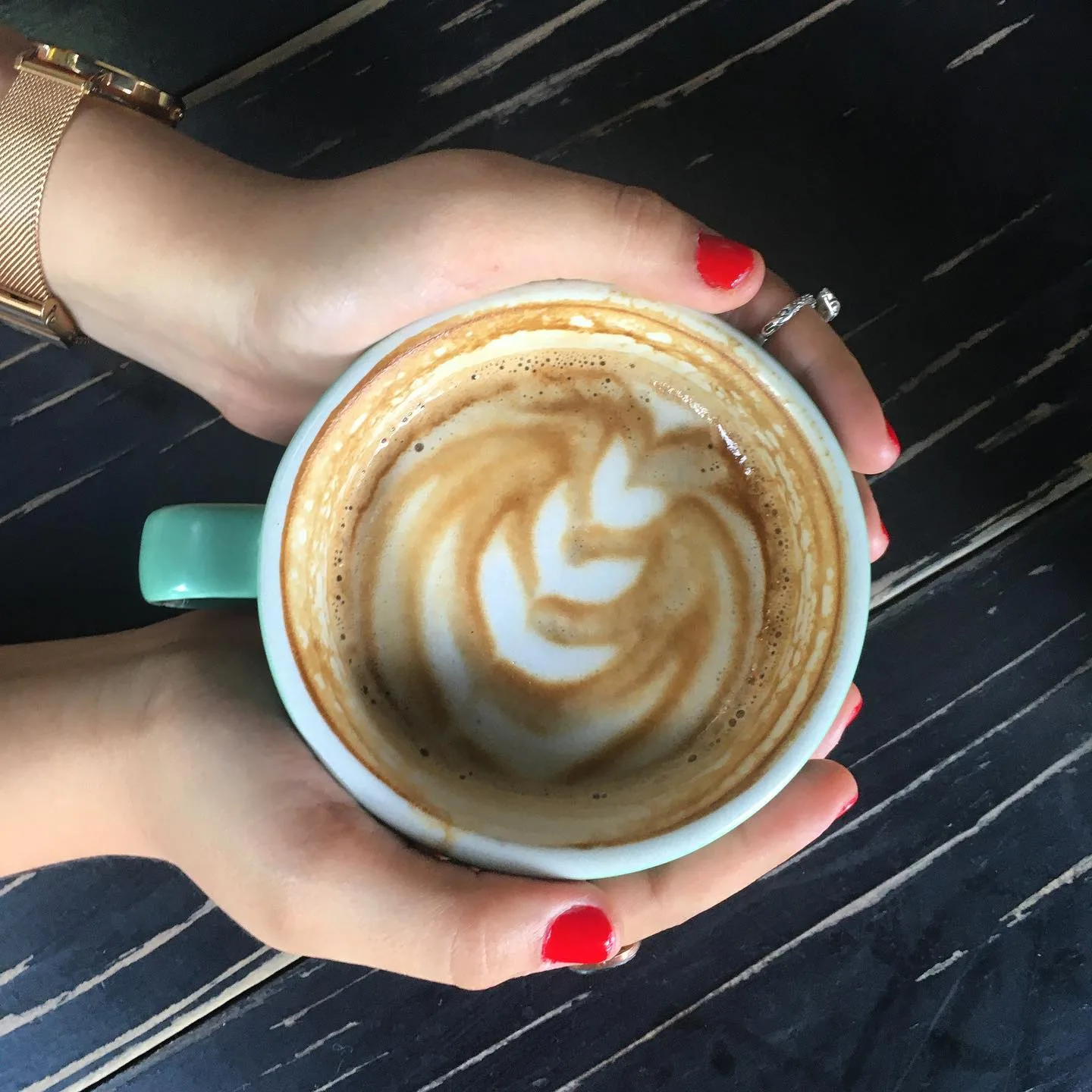 hand holding turquoise mug with latte art on dark wooden table., matraz tostador, guadalajara
