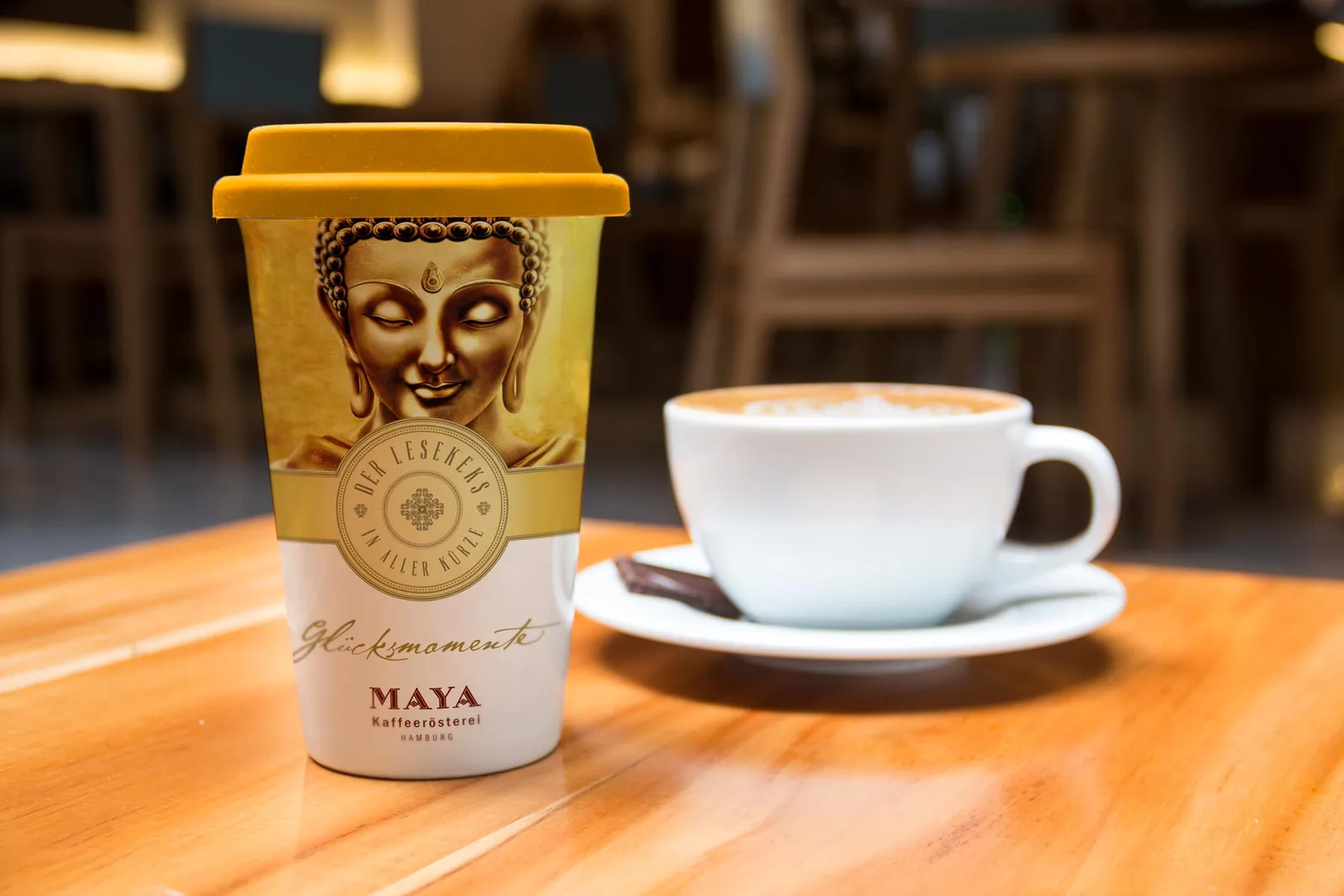 takeaway coffee cup with buddha design beside ceramic mug on wooden table., maya kaffeerösterei, hamburg