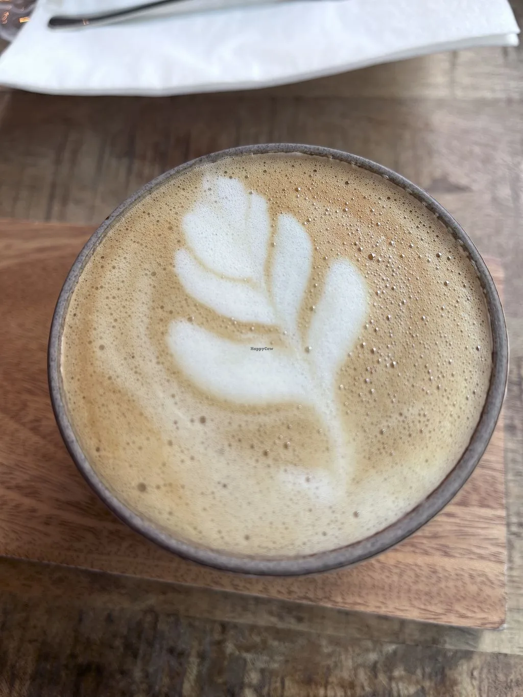 hand-poured leaf latte art in cappuccino with tan crema on wooden surface., meramanis coffee roaster, cologne