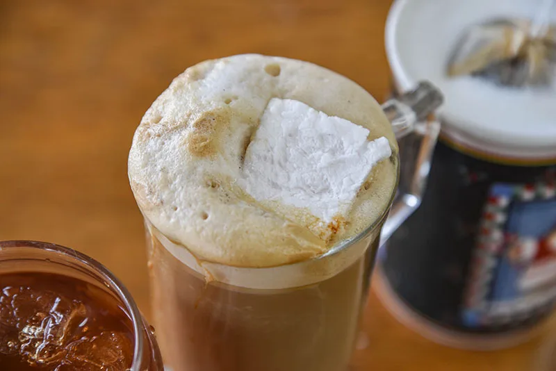 marshmallow-topped beverage in glass with caramel and condiments nearby., milestone coffee, montrose