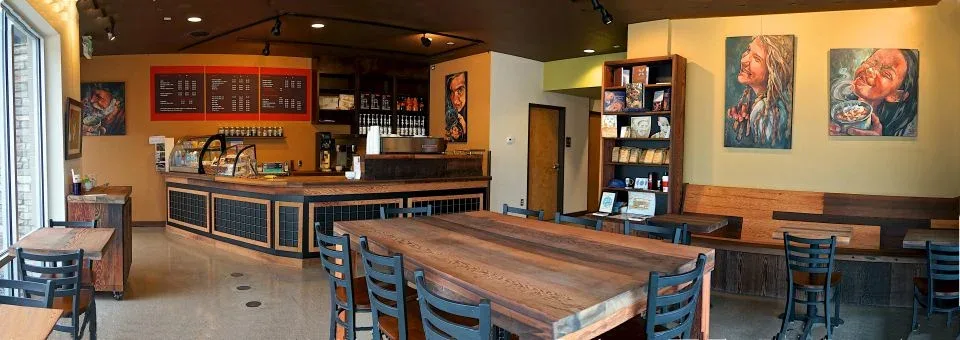warm coffee shop interior with wooden tables, counter service, and displayed artwork on walls., mission coffee roasters, inc.