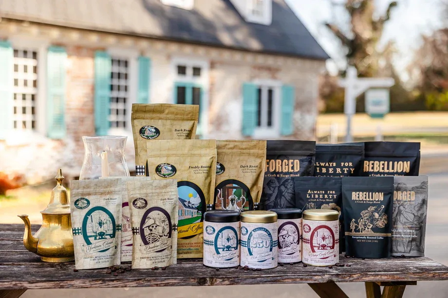 coffee products displayed on wooden table with colonial house and turquoise shutters behind., mobjack bay coffee roasters, yo