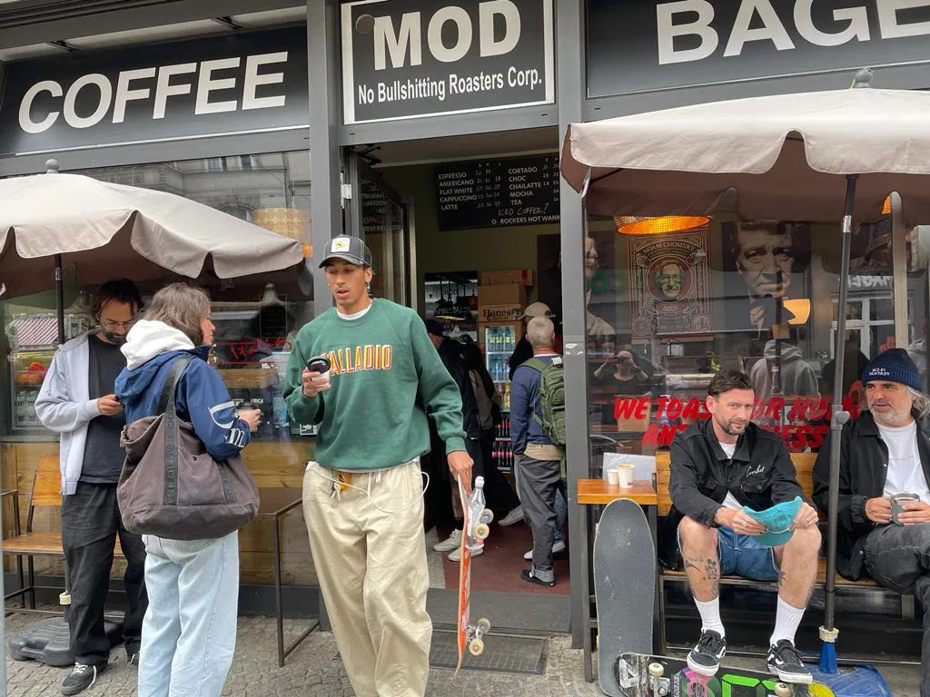 coffee shop storefront with customers, skateboarders sitting outside on bench., mod rockers roastery & bagels, berlin