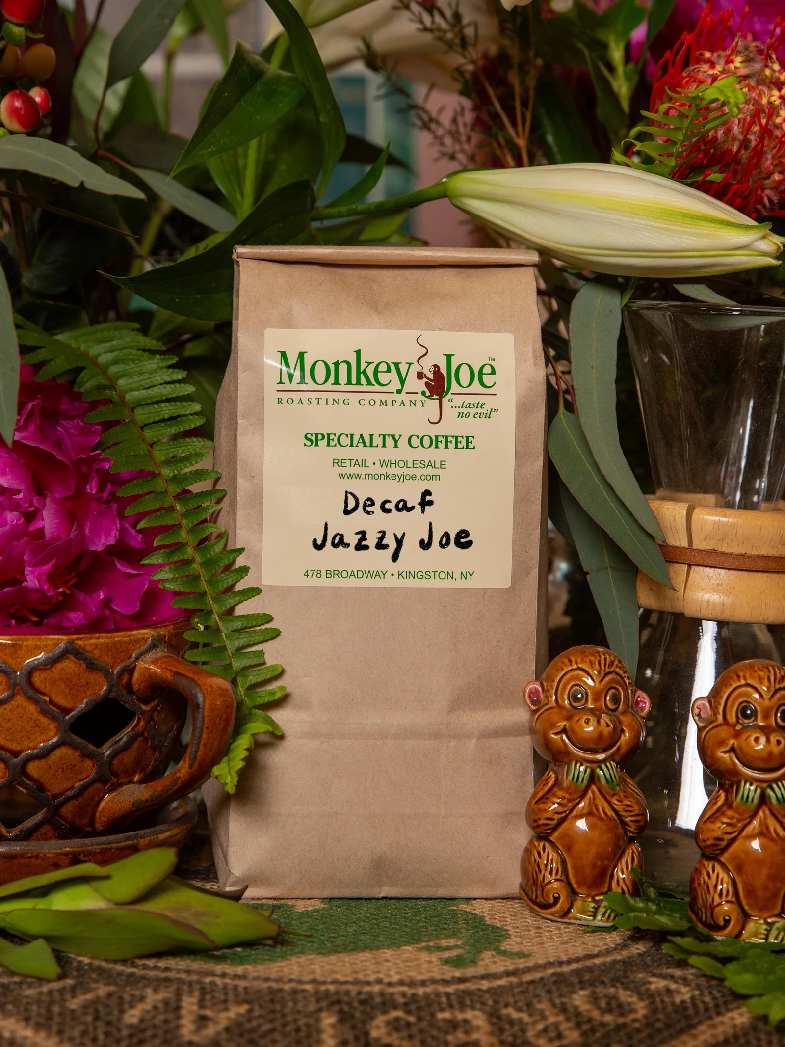 monkey joe decaf jazzy joe coffee bag surrounded by flowers and decorative monkey figurines., monkey joe roasting company, ki