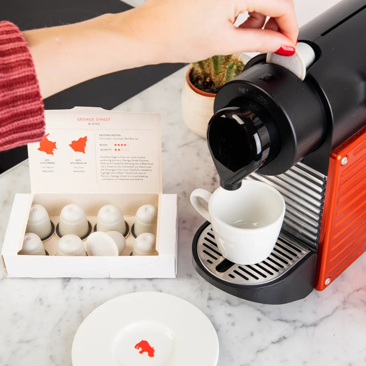 woman brewing coffee with capsule machine, george street blend box, marble countertop setup., mr. pod - the happiest coffee t