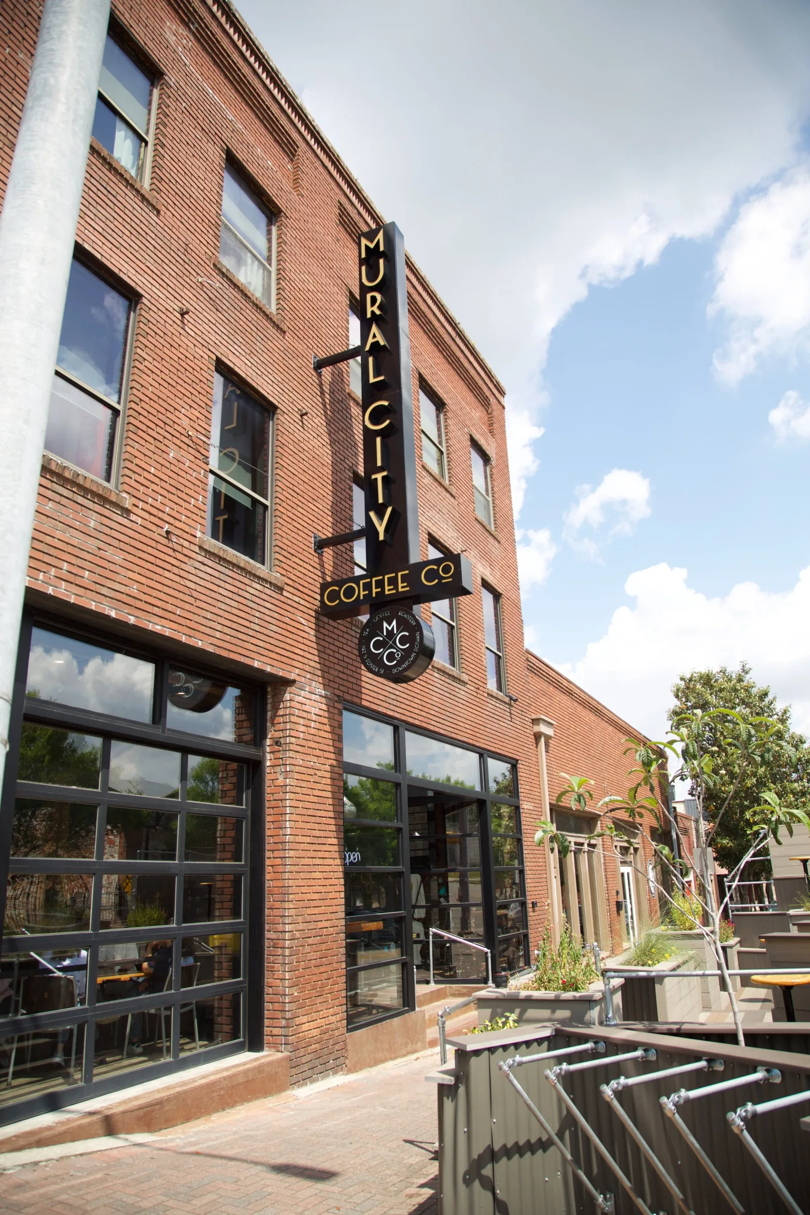 mural city coffee co storefront with black windows and vertical signage on brick building., mural city coffee company, alabam