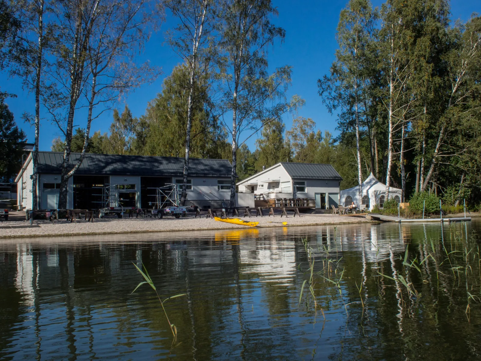 waterfront cottages with birch trees, yellow kayak, calm reflective water., natura viva | vuosaari paddling center, helsinki