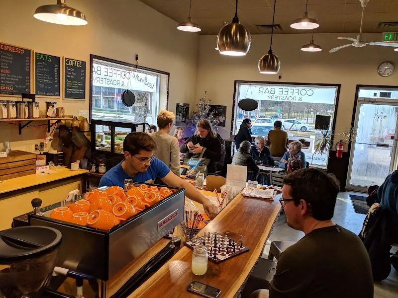 busy café with donuts, chess game, and customers by large windows., needmore coffee roasters, bloomington