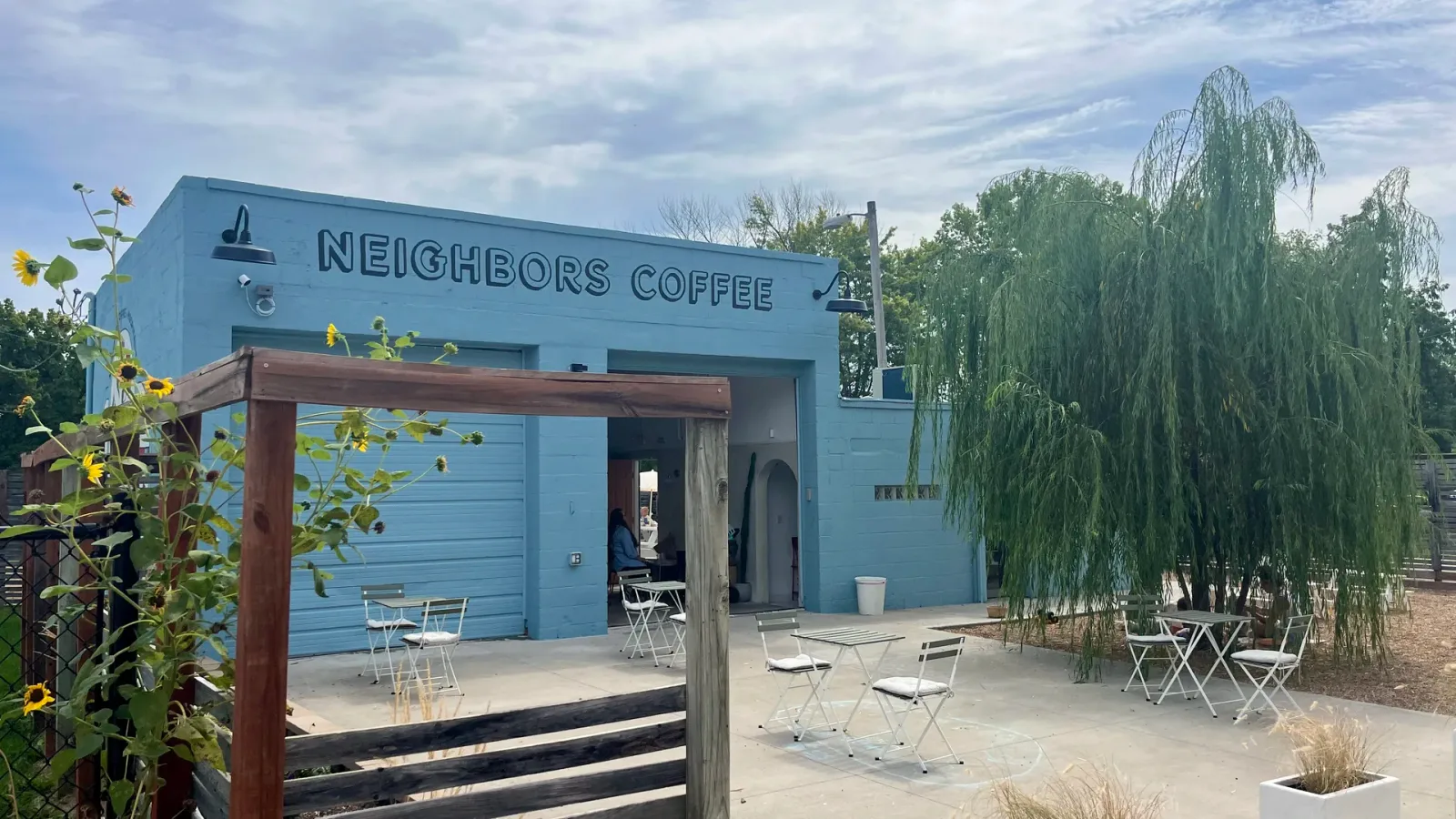 blue coffee shop with patio seating, sunflowers, and weeping willow trees., neighbors coffee & hospitality, kansas city