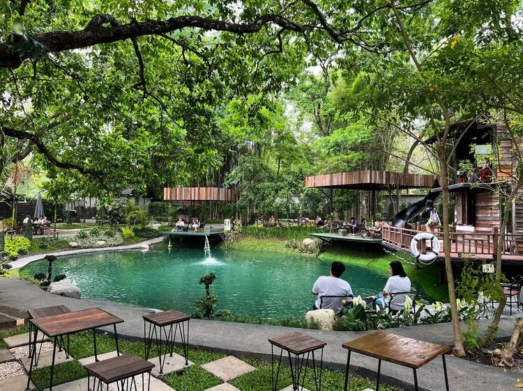 serene public park with turquoise pond, wooden structures, and lush trees overhead., nida's coffee shop, chiang mai