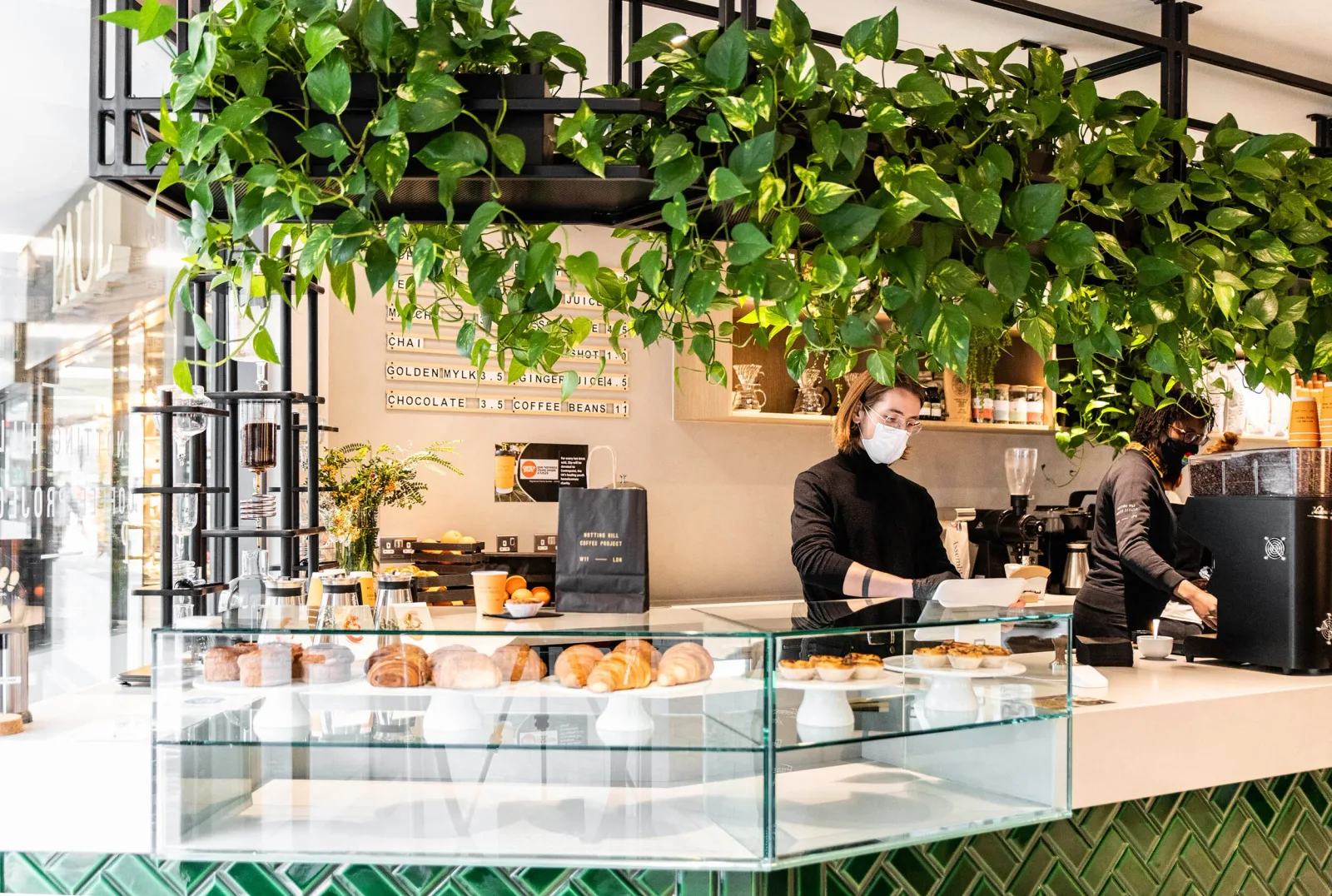 modern café interior with glass pastry counter, hanging plants, and masked staff members., notting hill coffee project, londo
