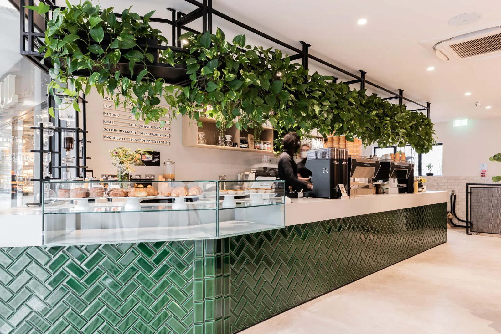 modern café interior with green tile counter, hanging plants, and pastry display case., notting hill coffee project, london