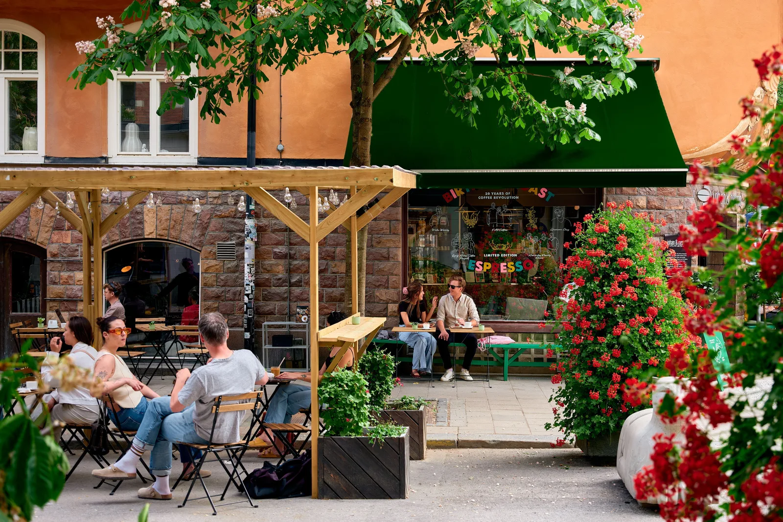 charming outdoor café with flowering plants, wooden awning, and seated patrons., nymble, stockholm